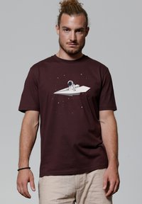 Bordeaux katoenen t-shirt met een afbeelding van een astronaut op een papieren raket tegen een sterry achtergrond. Korte mouwen en een losse pasvorm.