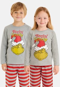 Le magliette a maniche lunghe grigie presentano il grafico del Grinch con il testo rosso e giallo "Feelin' Grinchy". I pantaloni del pigiama hanno righe alternate rosse e grigie.