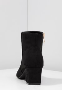 Sorte ruskinds ankelstøvler med blokhæl, der har en sidelukning og glat overflade, som fremviser et minimalistisk design og en struktureret form.