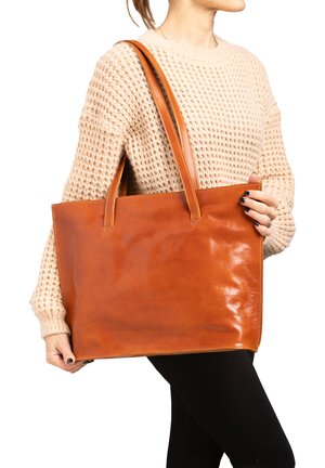 Tote-Bag aus elfenbeinfarbenem Leder mit glatter Textur, zwei Schulterriemen und Obernähten. Flache Form mit offenem oberen Teil, von einer Person in einem beigen Pullover gehalten.