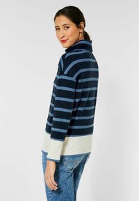 Marineblau und hellblau gestreifter Rollkragenpullover mit langen Ärmeln, mit einem helleren cremefarbenen Saum und weichem Stoffgefühl.