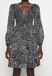 Černobílé šaty s výstřihem do V, dlouhými volánovými rukávy, smockovaným živůtkem, vrstevnatou sukní a abstraktní vzorovanou texturou.