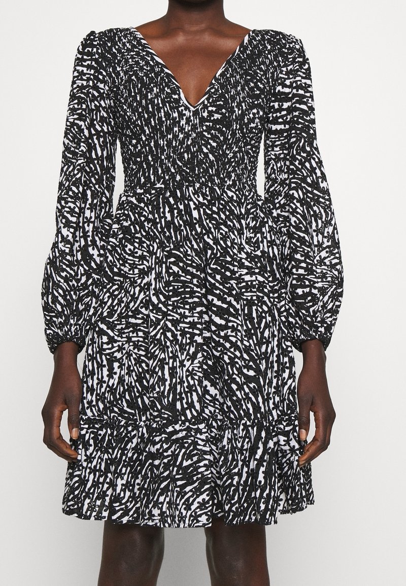 Černobílé šaty s výstřihem do V, dlouhými volánovými rukávy, smockovaným živůtkem, vrstevnatou sukní a abstraktní vzorovanou texturou.