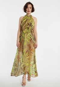 Robe maxi en tissu léger et translucide avec des motifs de feuilles vertes et brunes. Présente un col montant et une ceinture à la taille pour un ajustement réglable.
