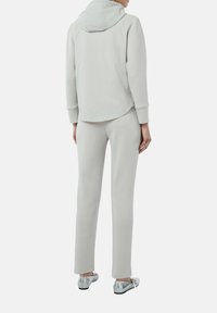 Jasno szara bluza z kapturem, długimi rękawami i luźnym krojem. Połączona z pasującymi jasno szarymi dresami i błyszczącymi srebrnymi balerinami.