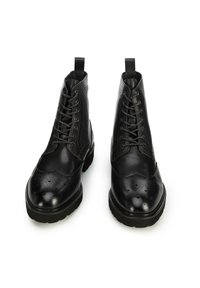 Botas de cuero negras hasta el tobillo con punteras redondas, perforaciones decorativas, diseño con cordones, lengüetas y suelas de goma texturizadas.