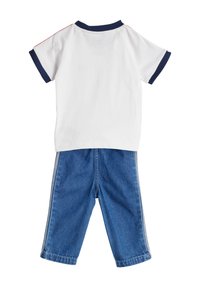 Balta medvilninė marškinėlė su tamsiai mėlynu apykakle ir rankovėmis, derinama su mėlynais džinsiniais kelnais su šoninėmis juostelėmis ir laisvu siluetu.