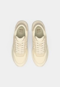 Baskets basses beige avec une tige en cuir lisse, une forme arrondie, un design à lacets et des semelles rembourrées, avec un discret détail de logo à l'intérieur.