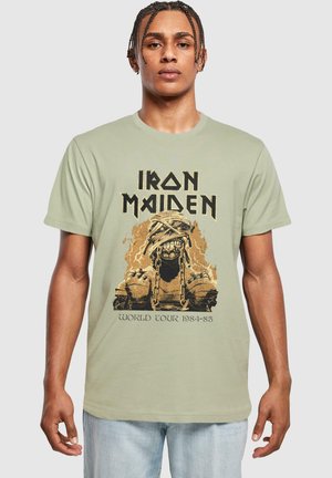 Lys grøn t-shirt i bomuld med et grafisk motiv af en indhyllet figur med kæder, samt "IRON MAIDEN WORLD TOUR 1984-85" i fed sort skrift.