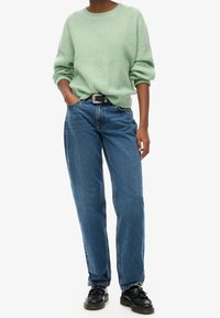 Ljusgrön stickad tröja med rullade ärmar, i kombination med högmidjade blå jeans. Svart bälte med silverspänne och svarta skor.