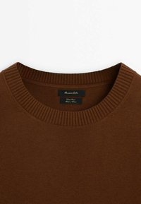 Bruine gebreide trui met een geribbelde ronde halslijn. Voorzien van een label met de naam "Massimo Dutti", dat de oorsprong van de stof en onderhoudsinstructies aangeeft.