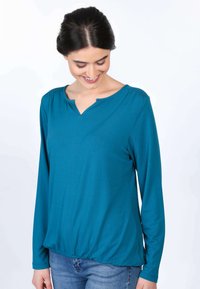 Türkise Langarmbluse mit rundem Halsausschnitt, sanften Raffung an den Schultern und einem lockeren Bund. Weicher, elastischer Stoff ohne sichtbare Muster.