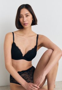 Zwarte kanten bh met een diepe V-hals en verstelbare bandjes, gecombineerd met bijpassende kanten high-waisted slipjes die verfijnde bloemmotieven benadrukken.