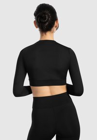 Schwarzes langärmeliges Crop-Top mit einer figurbetonten Passform, glatter Textur und einem bändigen Saum. Kombiniert mit passenden High-Waist-Leggings.