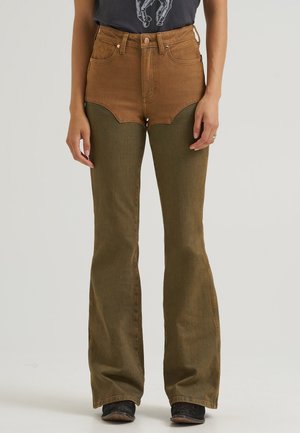 Femme portant un jean flare taille haute marron et vert olive avec poches avant, debout, les bras relâchés le long du corps.