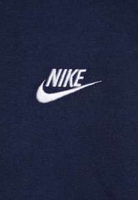 Mörkblått tyg med en mjuk textur som har en vit broderad Nike-logga och swoosh, placerad i det övre vänstra hörnet.