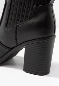 Bottine noire en cuir avec panneaux latéraux nervurés et talon épais texturé. Fini lisse avec détails de coutures renforcées.