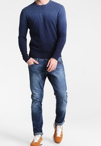 Marinblått stickat tröja med rund hals, kombinerad med ljusblå jeans och orange sneakers. Har en figursydd design och ribbad ärmslut.