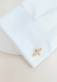 White cotton cuff with a textured pattern and a gold rectangular cufflink. The cuff's edge is neatly stitched and folded.