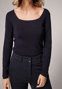 Haut noir à manches longues avec un col carré, une texture côtelée et une coupe ajustée, associé à un pantalon noir avec deux boutons à la taille.