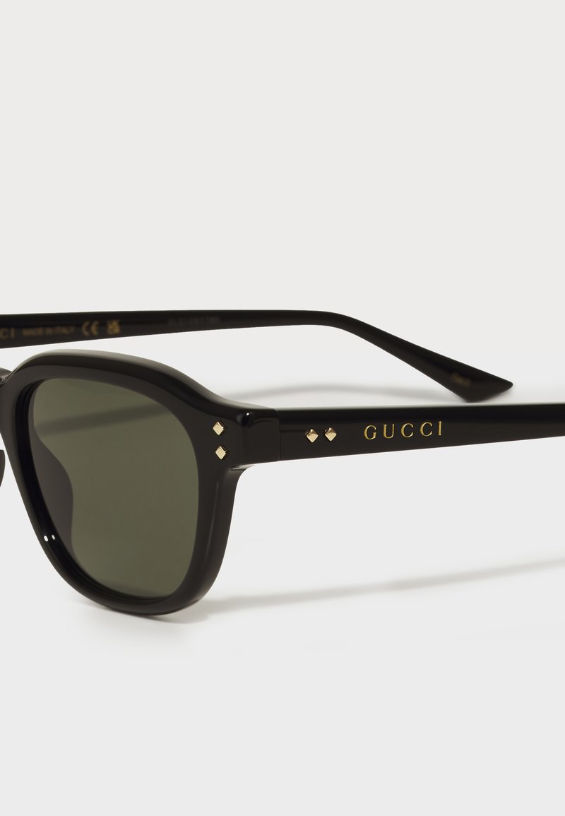 Lunettes de soleil noires avec des verres sombres. Présentent des accents dorés et de petites appliques en forme de diamant sur la monture. Fabriquées en plastique léger.