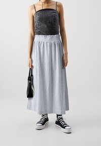 Top de mezclilla negra con tachuelas plateadas, falda maxi de rayas azules y blancas, bolso negro, zapatillas negras. Atuendo casual con texturas variadas.