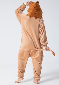 Brown plush lion onesie with a hood featuring a textured mane, tail, and front pockets. Soft fabric, relaxed fit, full-length sleeves and legs.