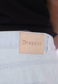 Light blue denim jeans with a tan leather tag labeled "Dropsize," featuring stitched accents and a smooth texture.