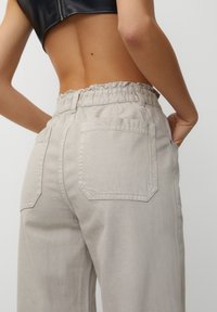 Pantalons gris clair taille haute avec une ceinture élastique, dotés de deux poches arrière et d'un tissu lisse et texturé.