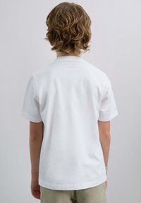 Camiseta de algodón blanca con mangas cortas, un cuello redondo y sin gráficos o patrones visibles, vista desde la parte de atrás.
