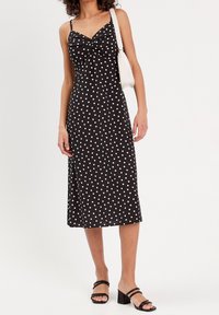 Sort midi-kjole med hvide polkaprikker, justerbare spaghetti-stropper, tætsiddende overdel med snoet detalje og udflaret kant. Kombineret med sorte hælede sandaler.