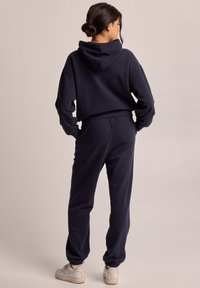 Navy blue hooded sweatshirt and matching joggers made of soft fabric. Features a cropped design and cuffed ankles. Worn with white sneakers.