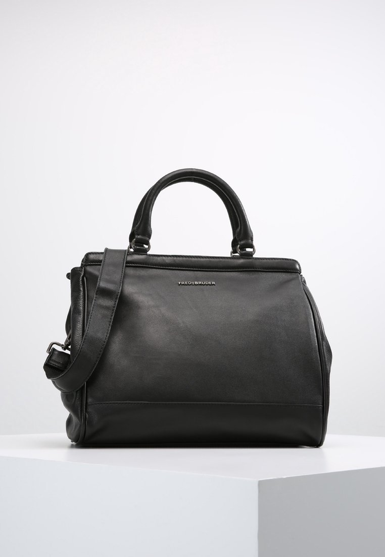 Sac à main en cuir noir avec doubles poignées et bandoulière amovible, posé sur un socle blanc sur fond uni.