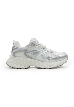 Zapatilla deportiva blanca y plateada con parte superior de malla, suela gruesa y acolchada, cordones y tira de sujeción en el talón, mostrada en perfil lateral.