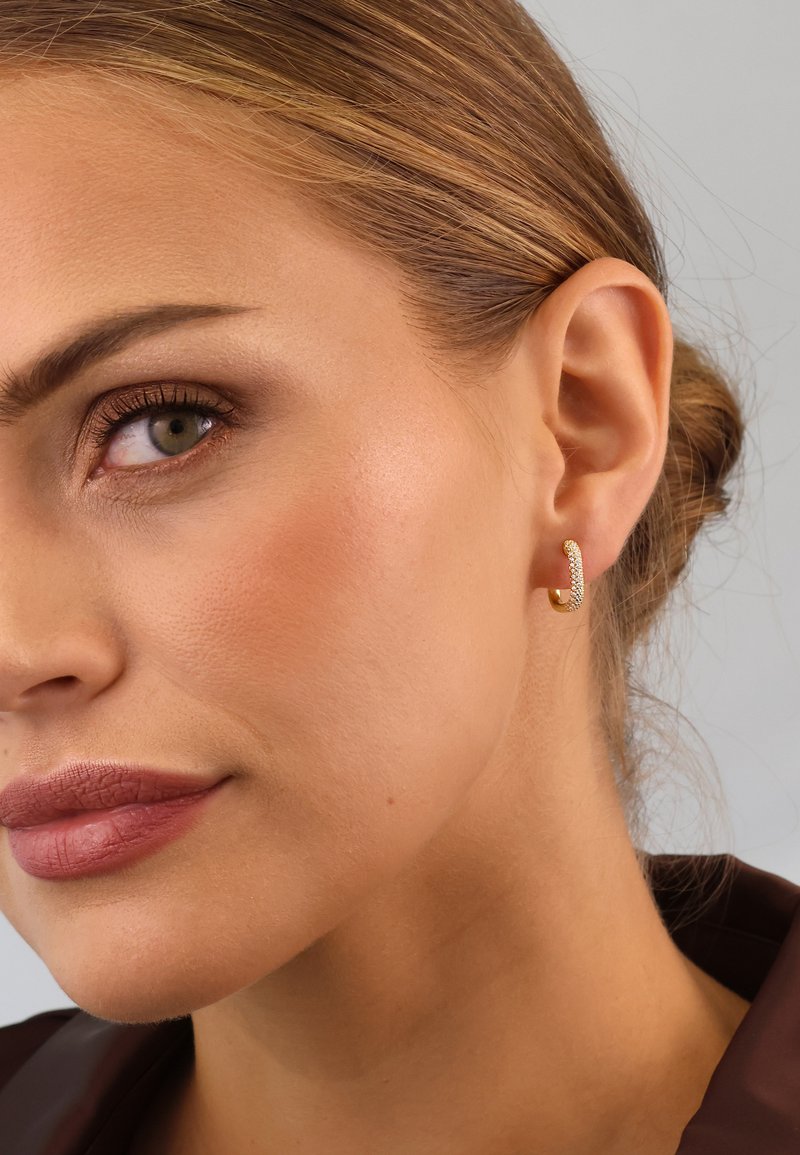 Gold hoop earring with a textured surface, featuring small embedded crystals for embellishment. Close-up view highlighting detail and fit.