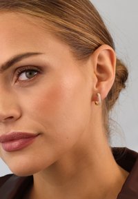 Gold hoop earring with a textured surface, featuring small embedded crystals for embellishment. Close-up view highlighting detail and fit.