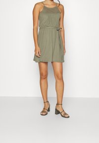 Zelené šaty ke kolenům s texturovaným tělem, tenkými ramínky a zavázaným pasem. V kombinaci s sandály na blokovém podpatku.