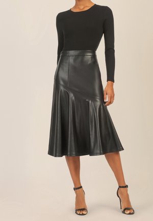 Femme portant un haut noir à manches longues, une jupe midi en cuir noire taille haute avec un ourlet évasé, et des sandales à talons hauts noires avec bride à la cheville.