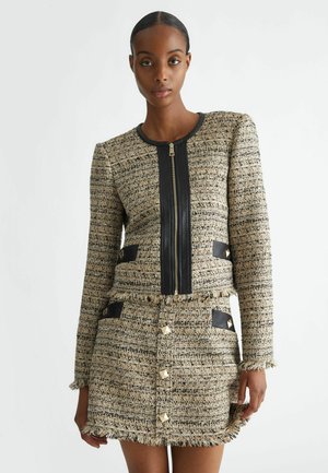 Tweed-Jacke mit schwarzen Lederdetails, Reißverschluss und fransigen Kanten; kombiniert mit einem passenden Rock mit goldfarbenen Knöpfen und Taschen.