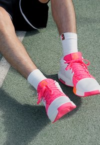 Sportske tenisice u bijeloj boji s jakim ružičastim naglascima i vezicama, s teksturiranim dizajnom i gumiranim potplatima, prikazane na teksturiranoj površini.