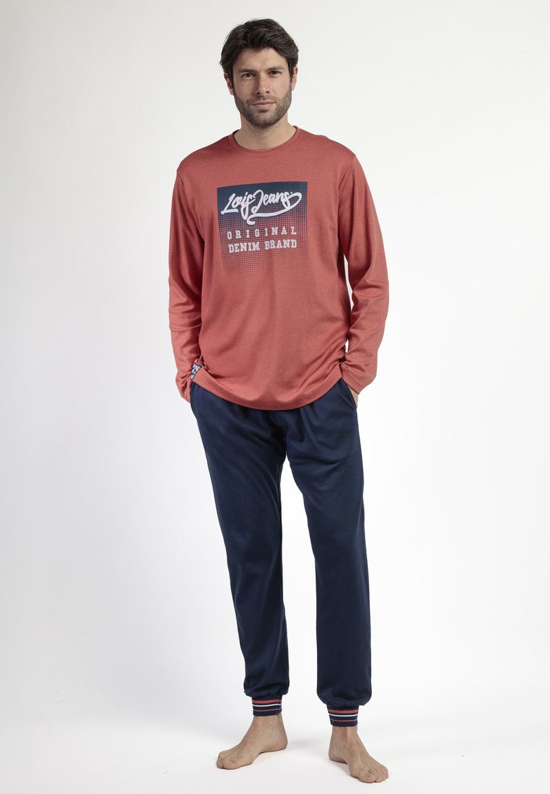 Camisa de manga larga de color óxido con un logotipo gráfico azul, combinada con pantalones deportivos navy con puños a rayas y bolsillos.