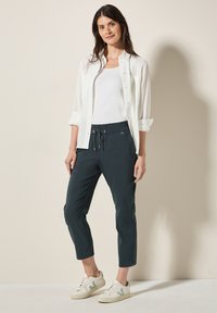 Pantalons de jogging vert foncé avec taille à cordon, associés à une chemise blanche rayée et des baskets blanches. Design plat et ajusté.