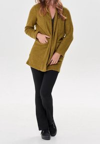 Senapsgul stickad cardigan med öppen fram, långa ärmar och sidofickor, tillsammans med svarta utsvängda byxor och svarta skor.