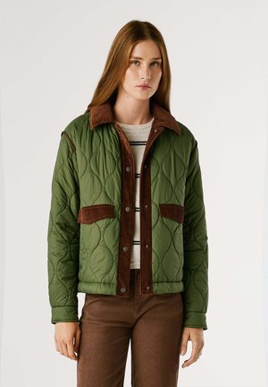 Gequiltede groene jas met bruin corduroy accents, drukknopen en opgestikte zakken. Gedragen over een gestreept sweater en bruine broek.