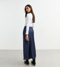 Vit långärmad topp i kombination med en flödande marinblå maxikjol och svarta klackstövlar; mjuk textur och ankellång design.