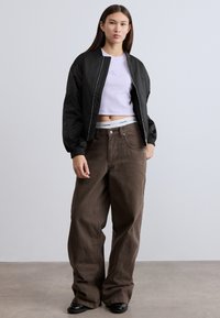 Μαύρο μπουφάν bomber με ριμπ μανσέτες, ανοιχτό μωβ κοντό τοπ και φαρδιά καφέ παντελόνια. Γυαλιστερά μαύρα παπούτσια ολοκληρώνουν την εμφάνιση.