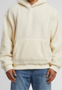 Felpa con cappuccio color crema in tessuto texturizzato, dotata di tasca frontale e orlo a coste. Il cappuccio è rivestito e le maniche sono a polsino.