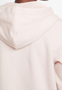 Sudadera con capucha de color rosa claro, con una textura suave y lisa; cuenta con una capucha grande y una zona cosida a lo largo del escote.