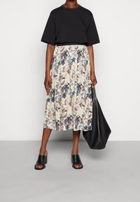 Svart kortärmad topp, blommig midiklänning i kräm, blå och rosa nyanser, klackskor i svart och en svart tote väska. Slät tygtextur.