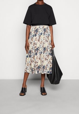 Haut noir à manches courtes, jupe midi fleurie dans des tons crème, bleu et rose, chaussures noires à talons et sac fourre-tout noir. Texture de tissu lisse.